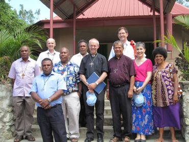 A group of ten people posing outside a building with tropical plants.