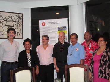 A group of seven people posing indoors near a poster and artwork.