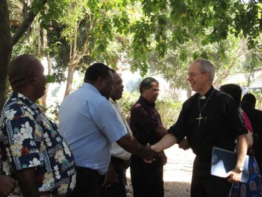 A group of men, including a religious leader, shaking hands outdoors.
