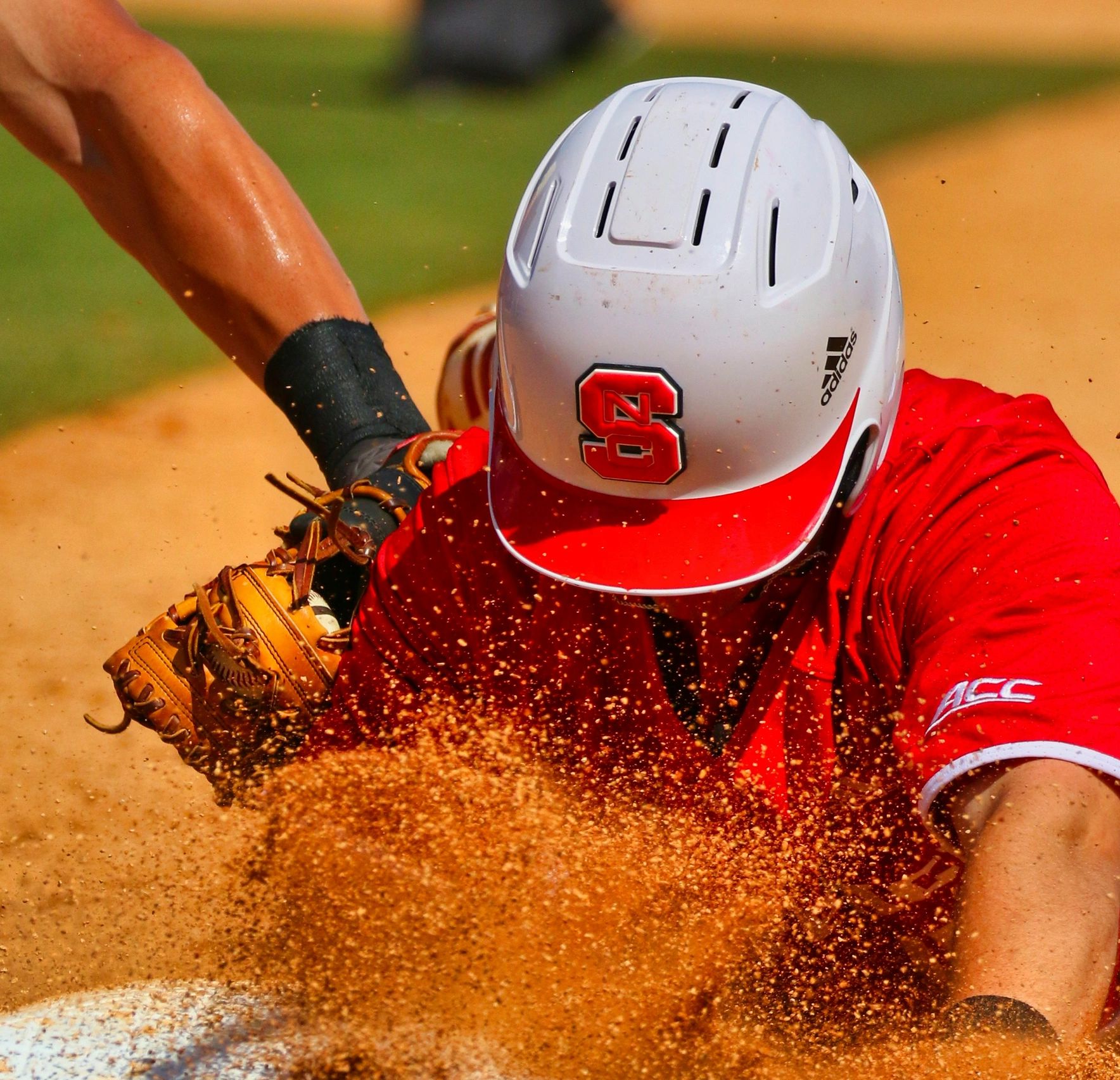 Baseball player sliding into a base, kicking up dirt.