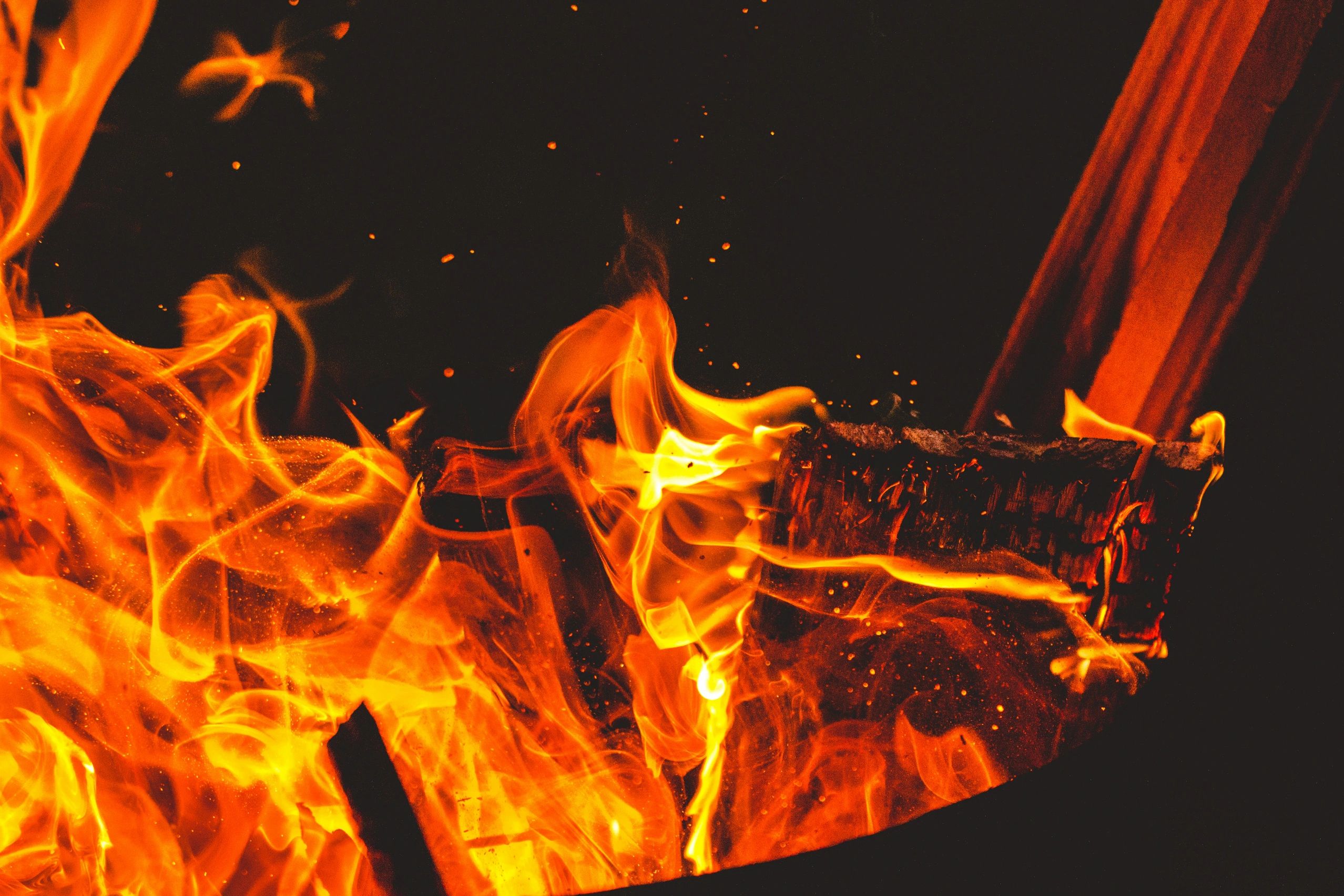 Close-up of bright orange flames consuming wooden logs in darkness.
