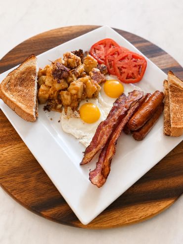 Classic breakfast with eggs, bacon, sausages, toast, potatoes, and tomatoes.