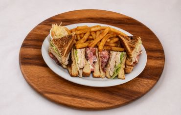 Club sandwich with fries on a wooden platter.
