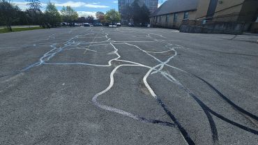 Pavement with long, winding cracks sealed with tar under a blue sky.