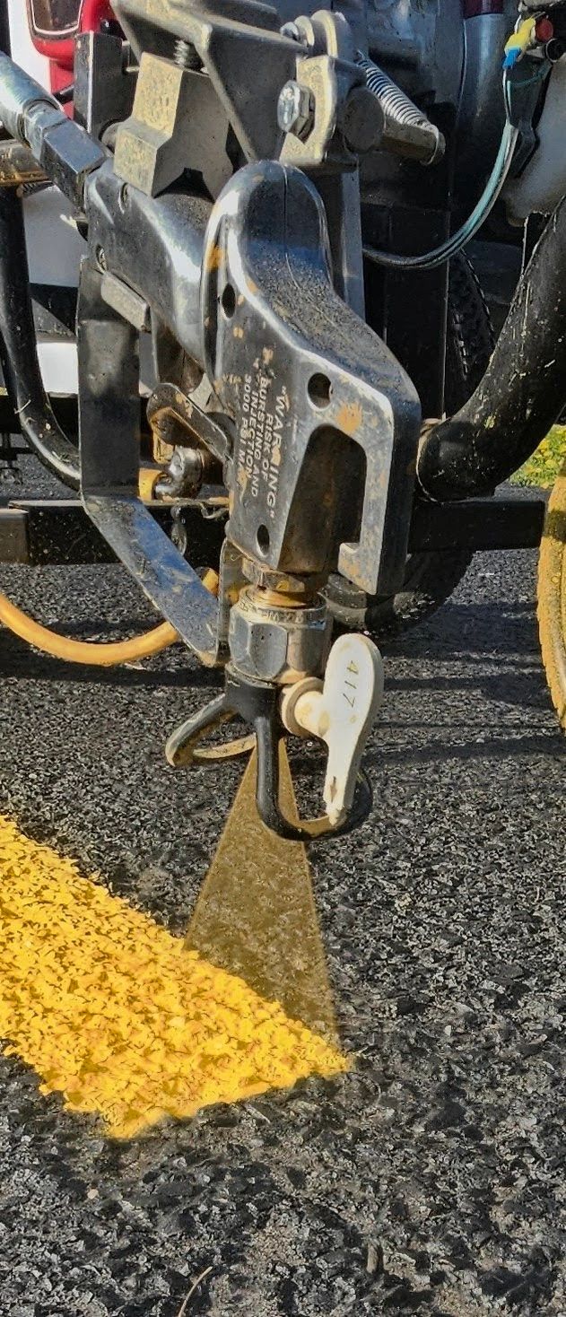 Close-up of a road line painting machine spraying yellow paint on asphalt.