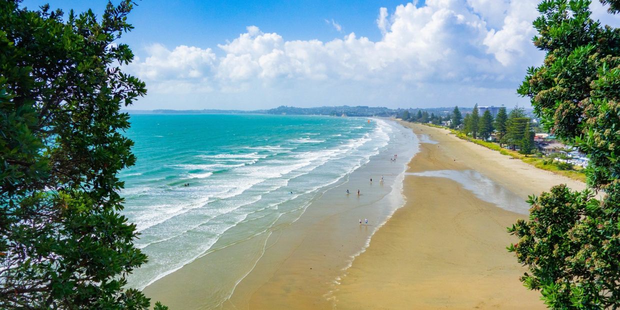 Wide beach view of the Hibiscus Coast with turquoise water and people walking.