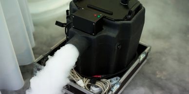 Fog machine emitting thick white smoke on a case with cables.