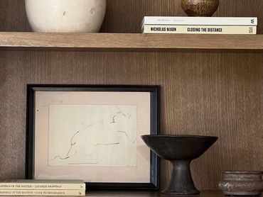 A minimalist sketch of a reclining figure on a wooden shelf with decorative objects.
