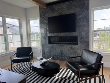 Modern living room with black leather chairs, a striped rug, and a wall-mounted TV above a fireplace.