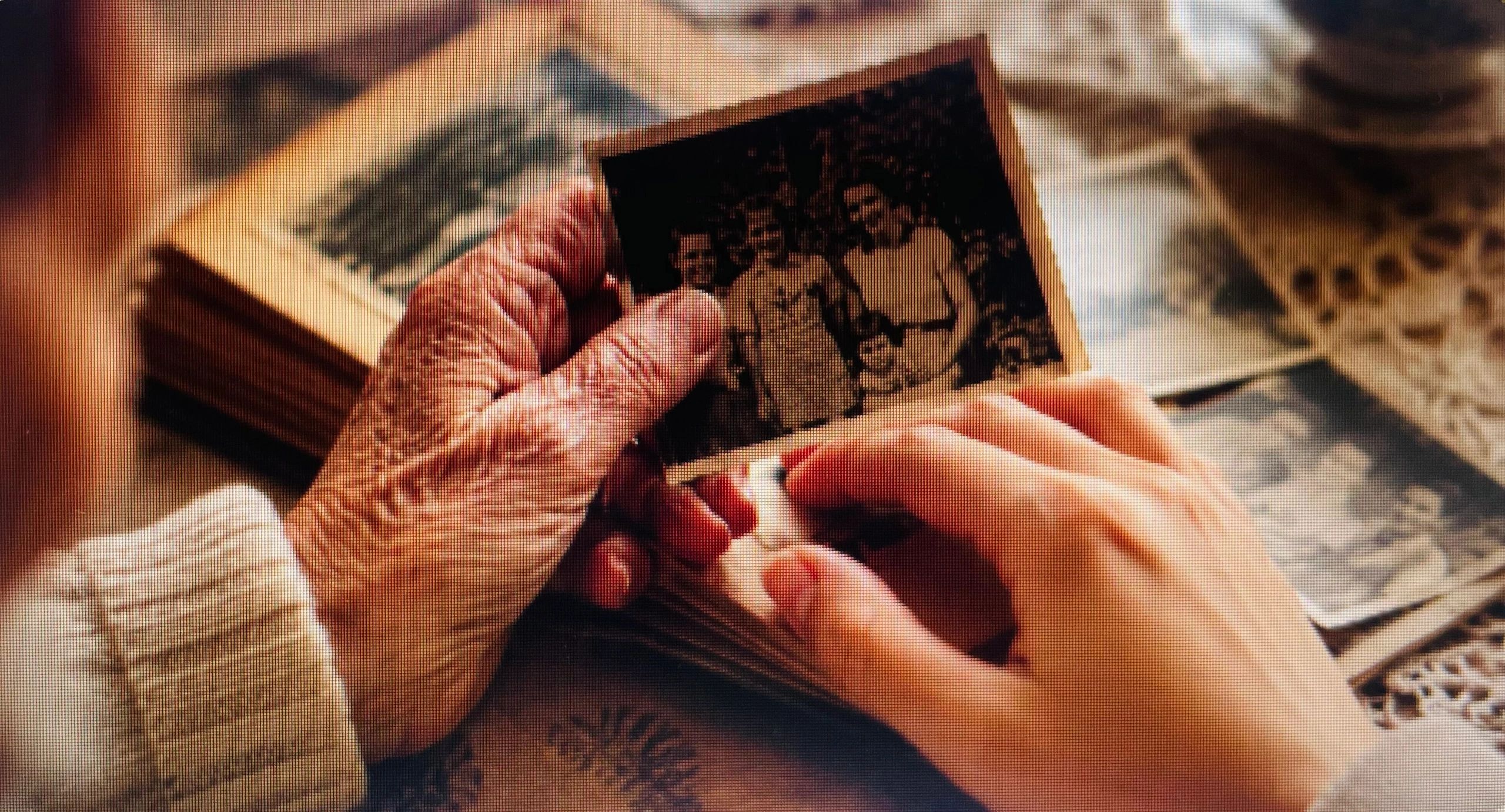 An elderly hand and a younger hand holding an old family photo together.