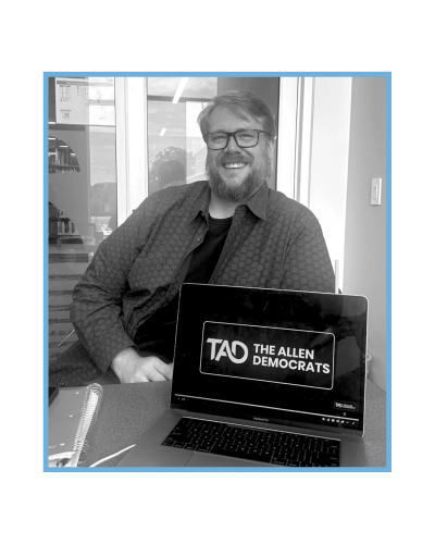 Man smiling behind a laptop displaying The Allen Democrats logo., Jeff Kinnear