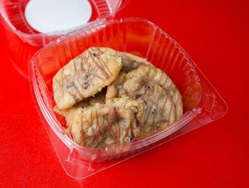 Chocolate-drizzled cookies in a plastic container on a red surface.