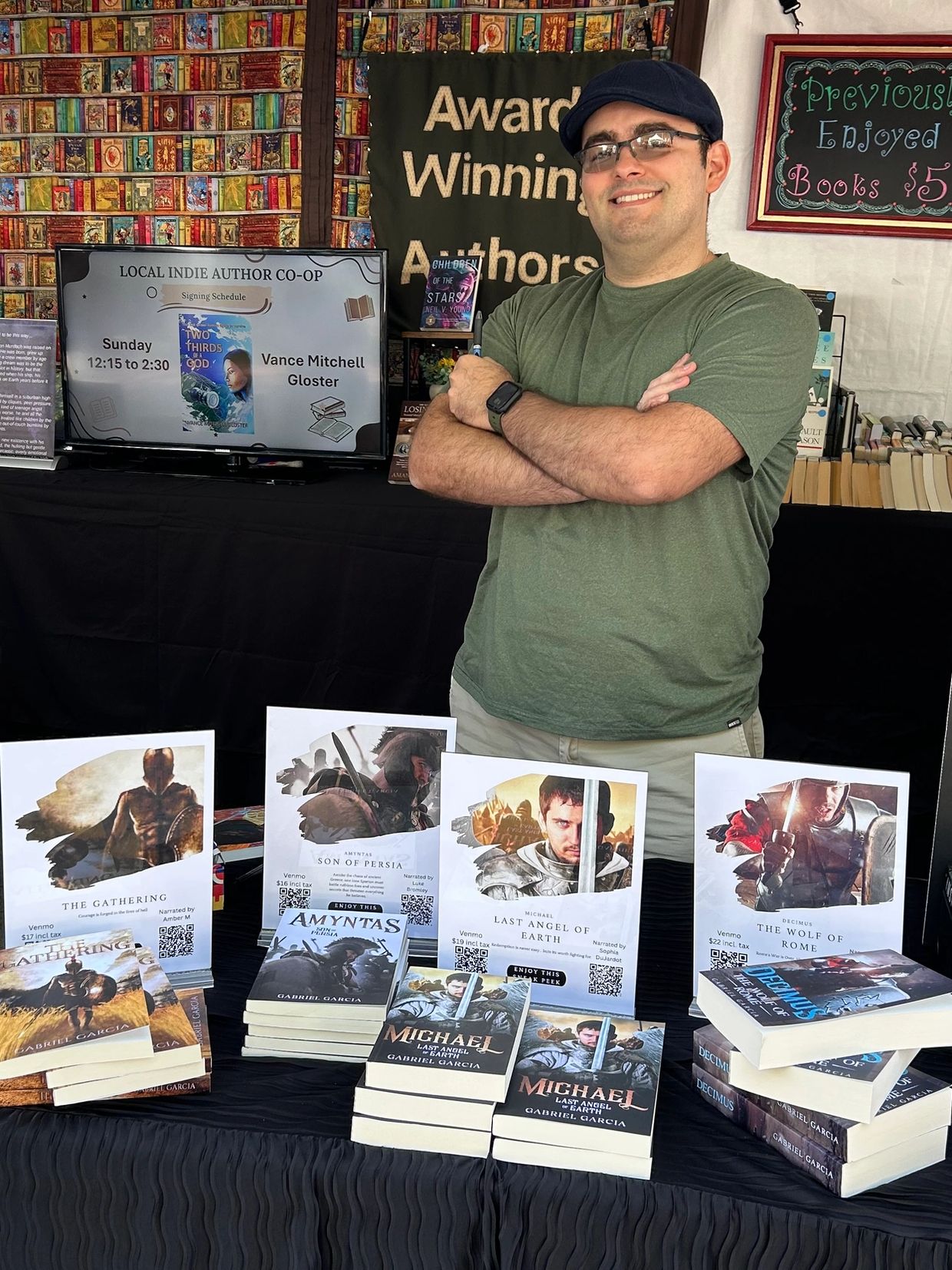 Man standing at a book booth with various fantasy novels displayed.