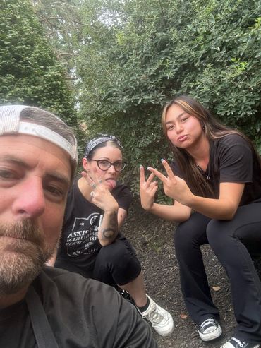 Three employees with goofy faces sit outside and pose for the camera. 