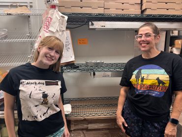 Two smiling employees stand before a wire storage rack.  