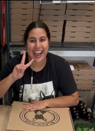 A friendly workers smiles and gives the peace sign at the front counter.  