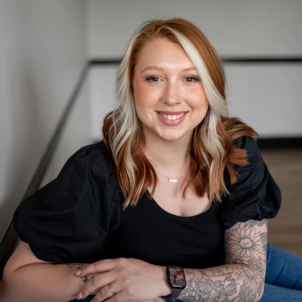 Smiling woman with blonde and brown hair and tattooed arm.