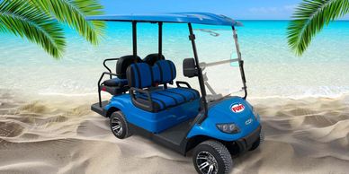 Blue golf cart parked on a sandy beach with palm leaves overhead.