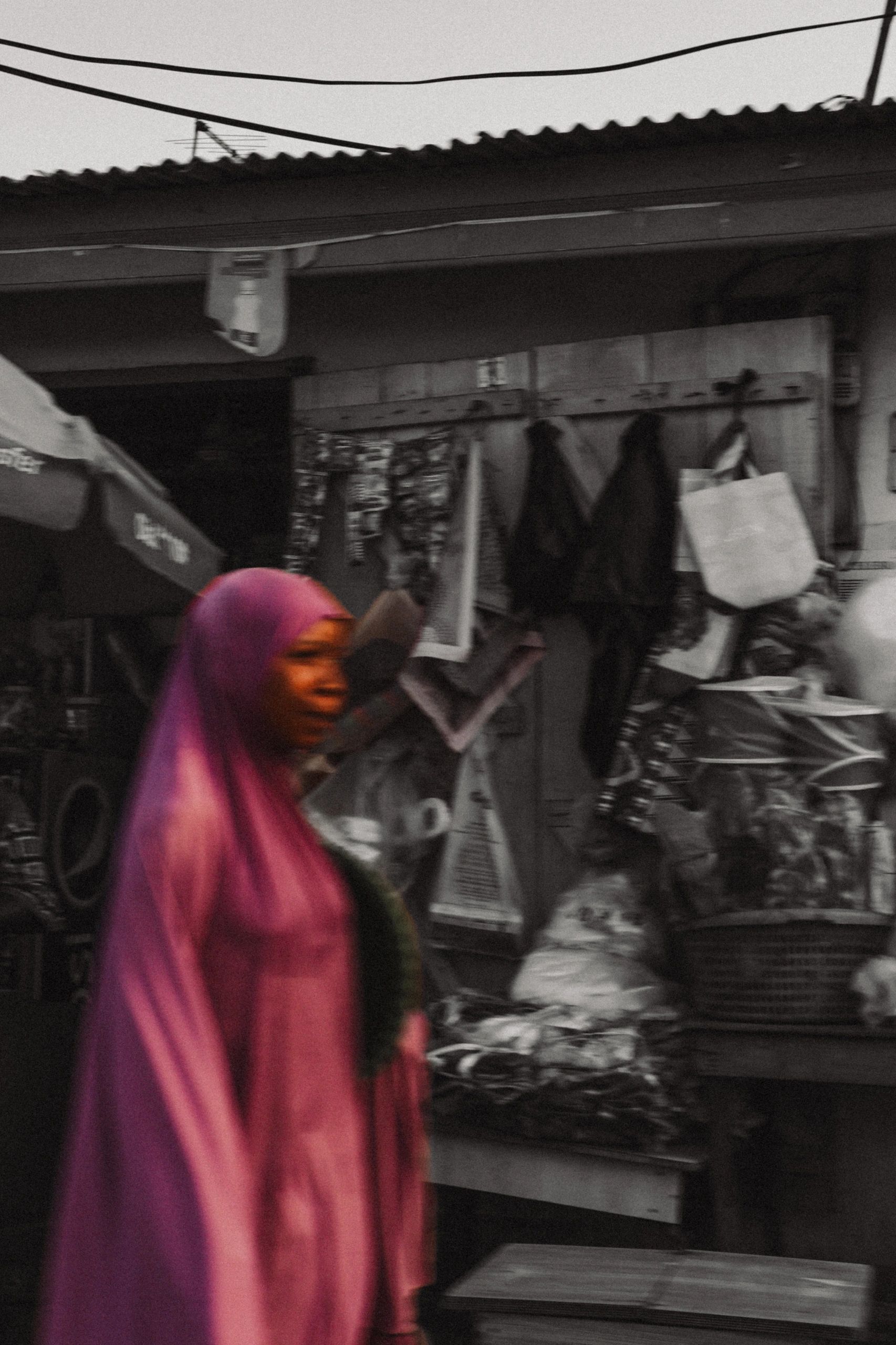 Woman in pink hijab walking past a market stall.