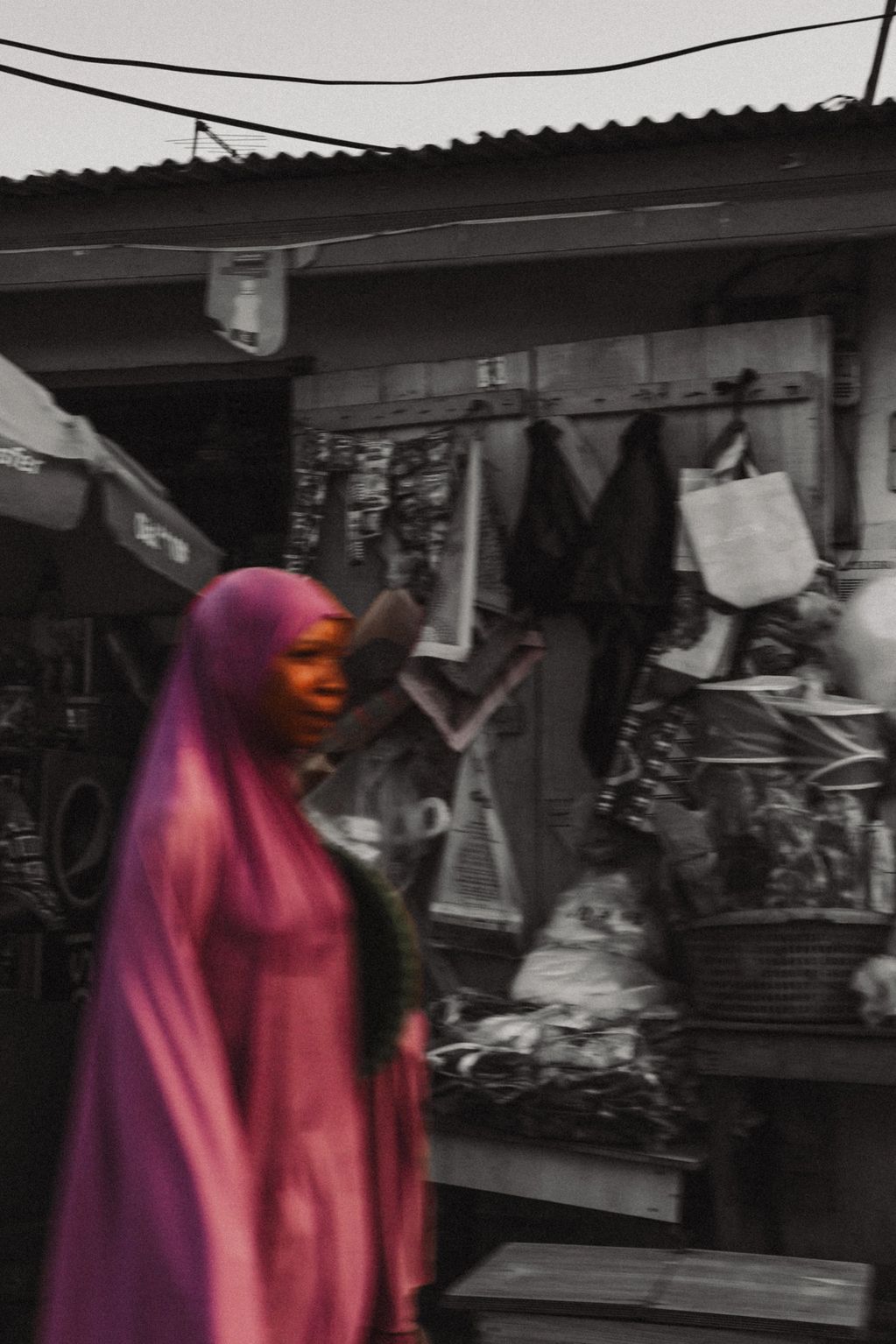 Woman in pink hijab walking past a market stall.