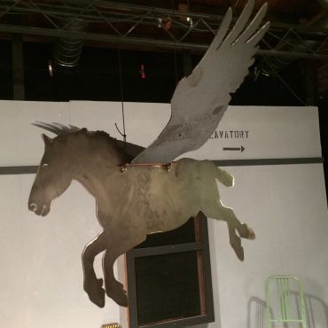 Metal sculpture of a winged horse hanging indoors.