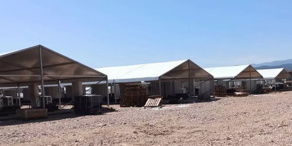 Rows of large white tents set up on a barren, rocky ground under a clear blue sky.