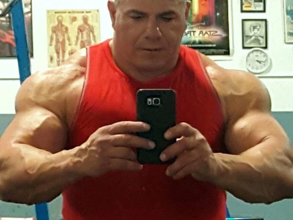Muscular man in red tank top taking a gym mirror selfie.
