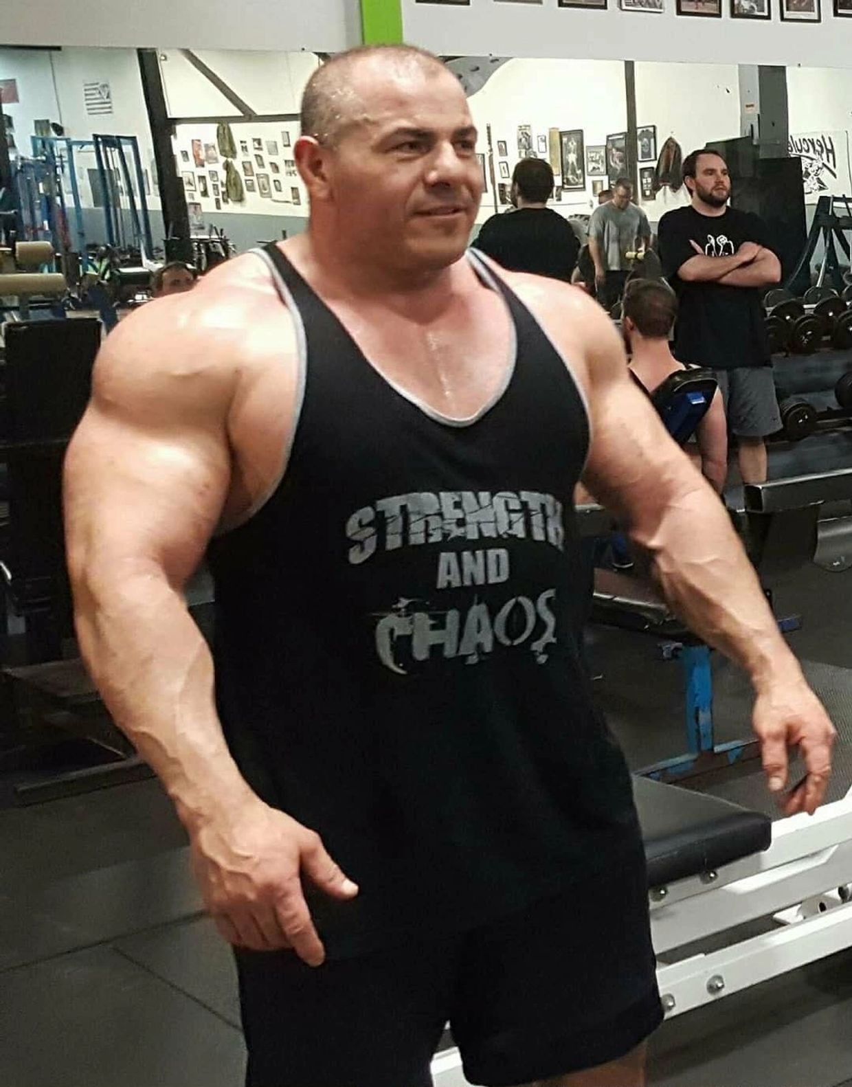 Muscular man in a gym wearing a 'Strength and Chaos' tank top.