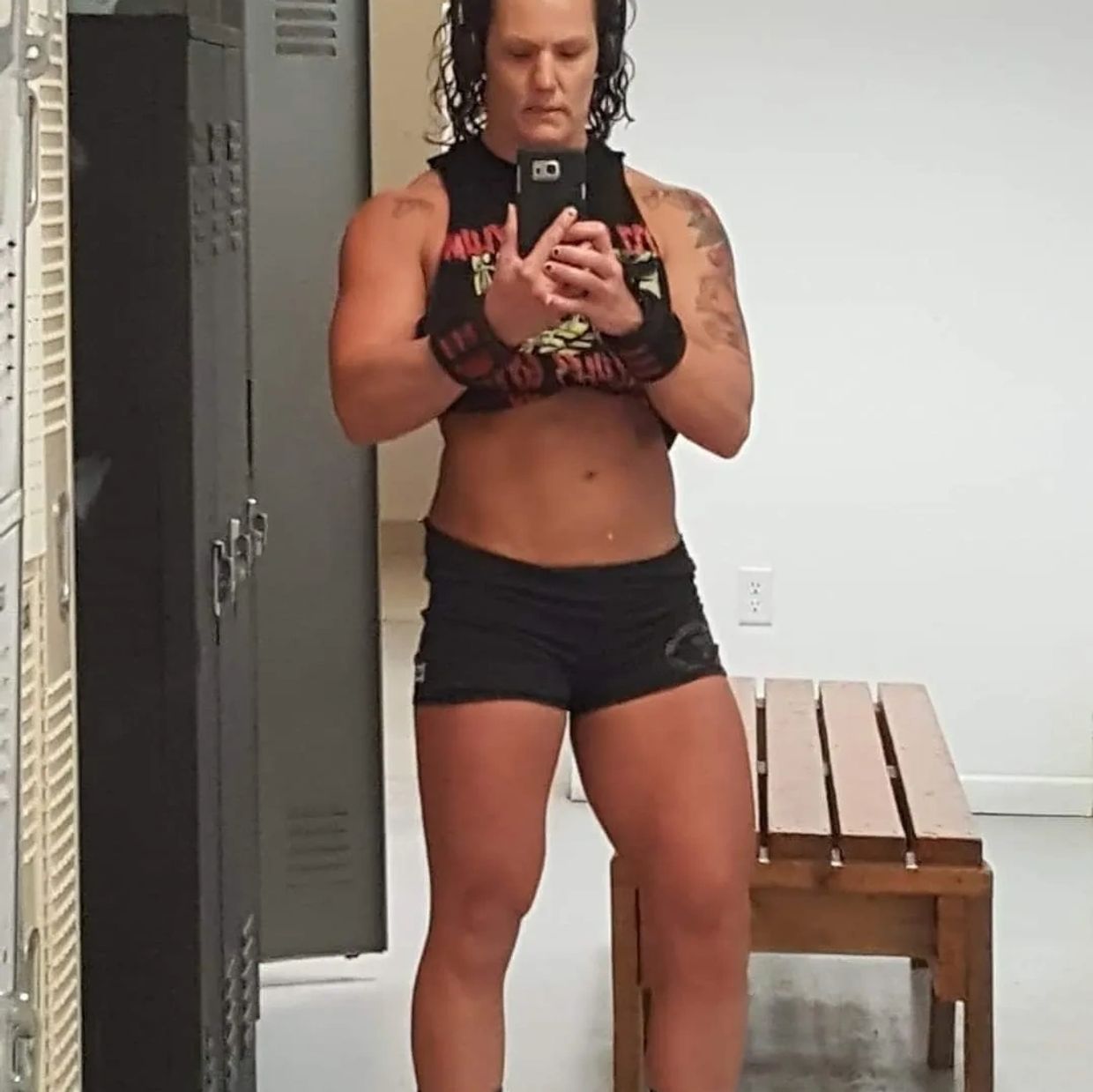 Muscular woman taking a selfie in a gym locker room.