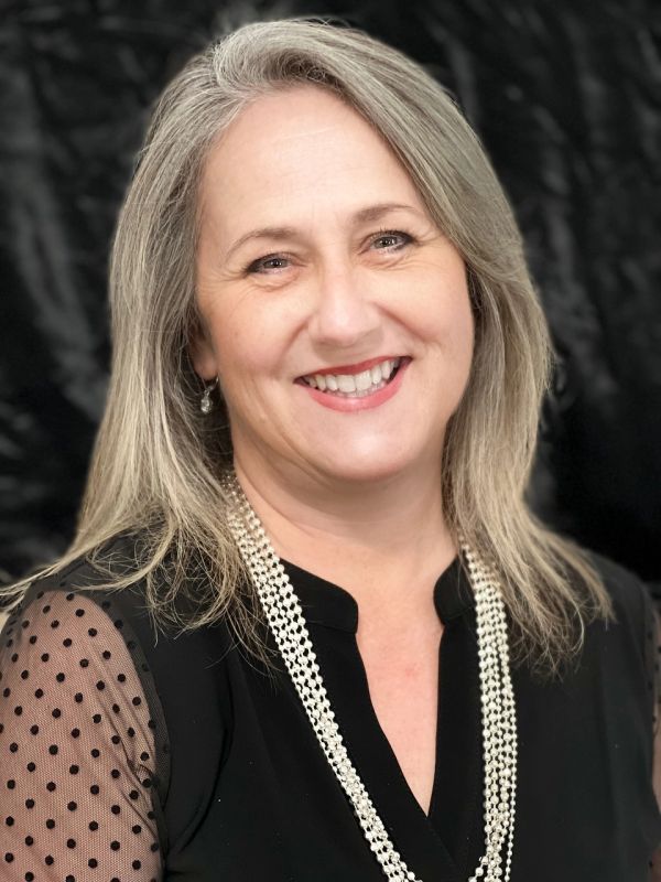 Smiling woman with gray hair wearing a black blouse and pearl necklace.