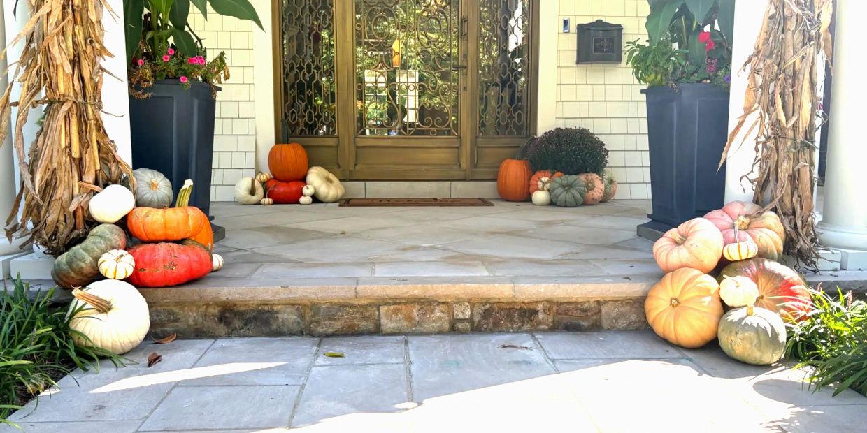 Front porch decorated with various pumpkins and dried corn stalks.