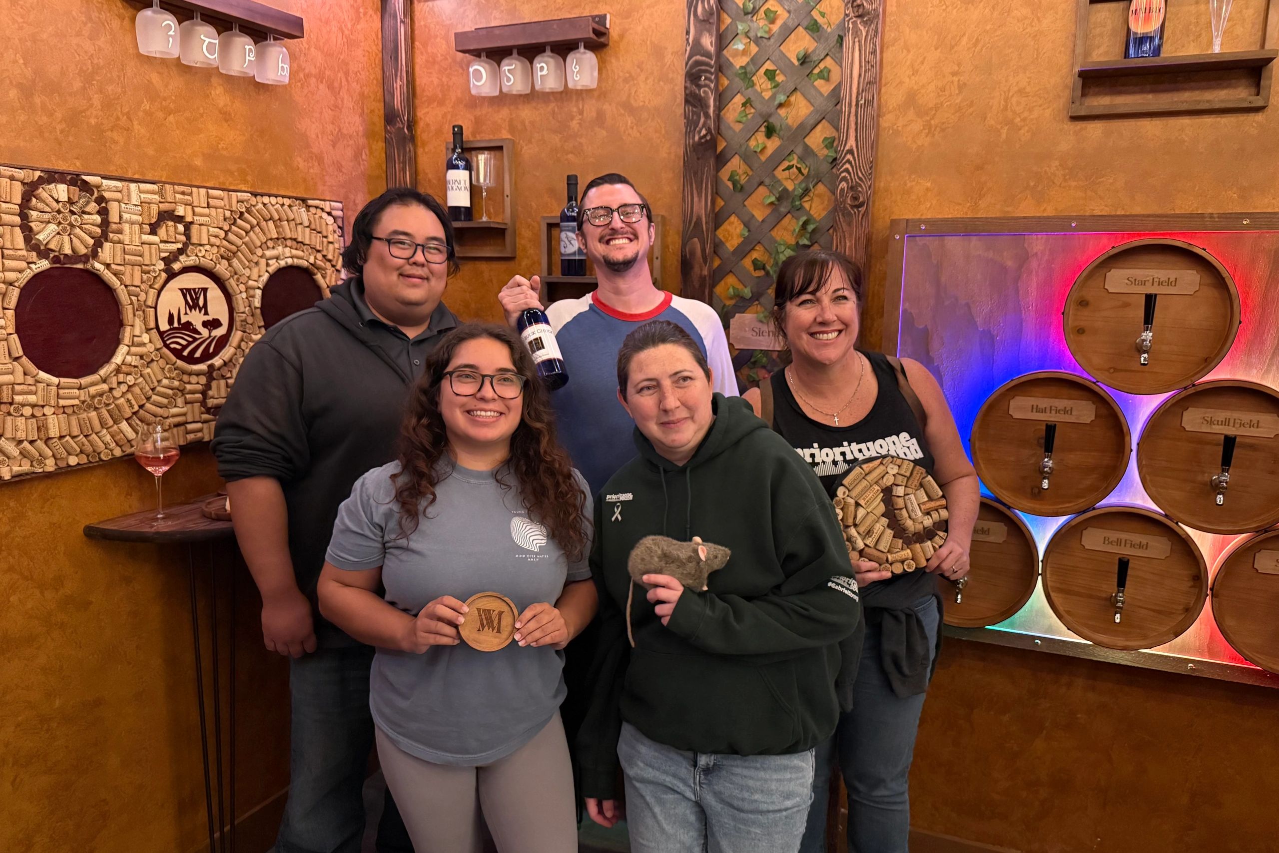 Group of friends smiling in a cozy wine cellar with wine barrels and cork decor.