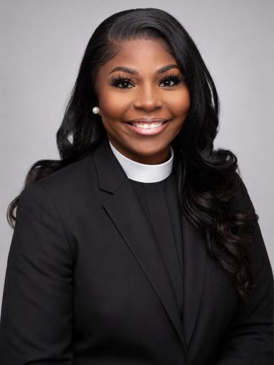 A smiling female clergy in black suit and white clerical collar.