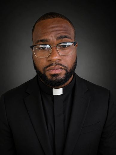 Portrait of a man in a priest collar and glasses.
