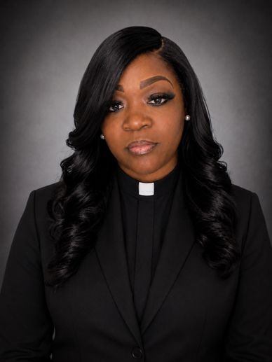 Portrait of a woman pastor with long curly hair and clerical collar.
