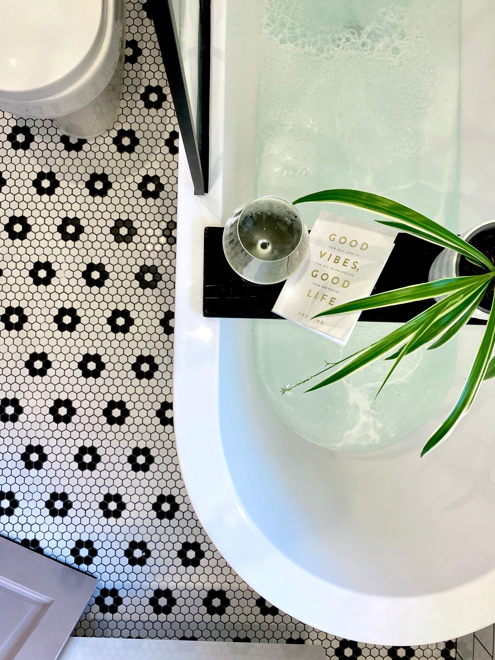 bathroom with penny tiles. daisy floor and monochrome vibes. bath tray with spider plant and wine