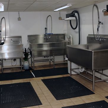 Commercial kitchen area with three large stainless steel sinks and black floor mats.