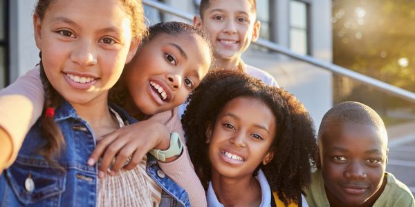 Group of diverse kids happily posing outdoors for a selfie at sunset.