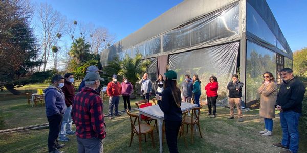 A group of people gathered outdoors near a large greenhouse on a sunny day.
