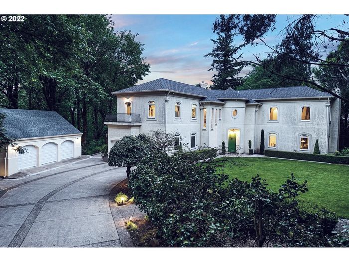 Elegant two-story house with a curved driveway and lush greenery at dusk.