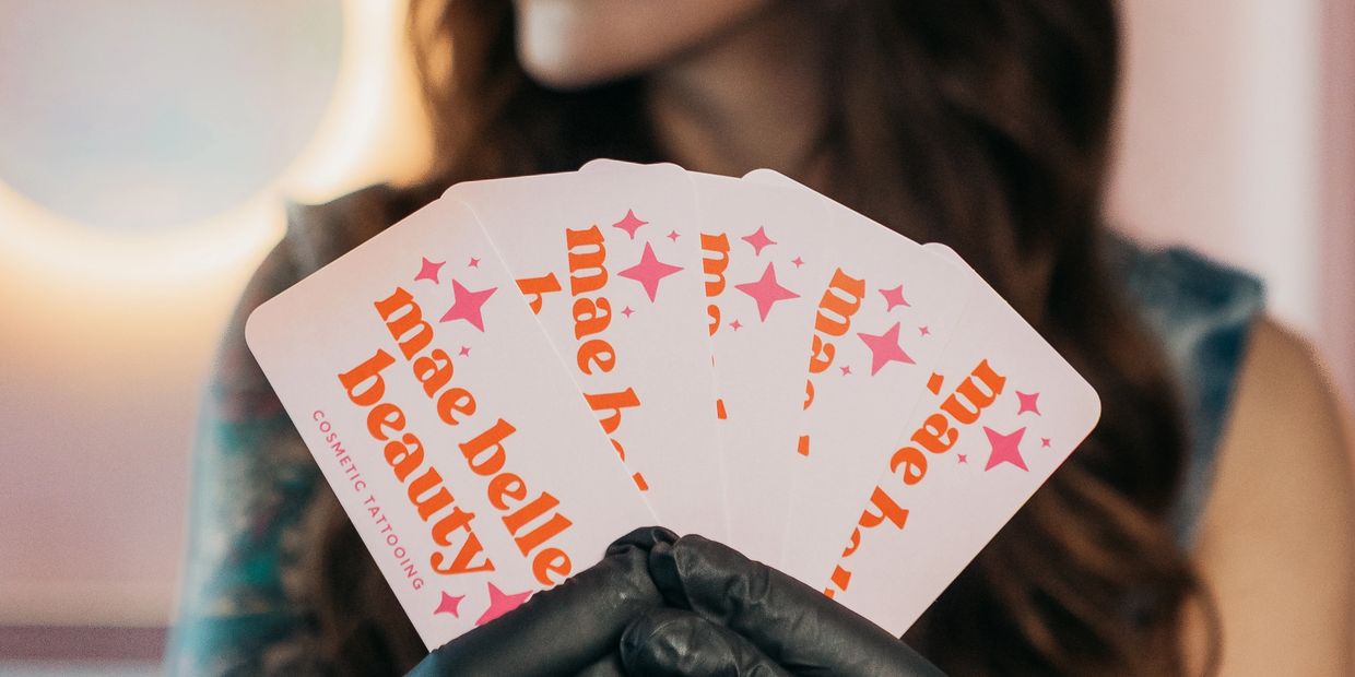 Person holding promotional cards for Mae Belle Beauty cosmetic tattooing.
