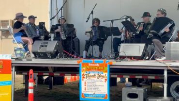 Accordion band performing on a small outdoor stage.