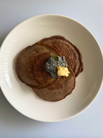 Three brown pancakes with dollops of butter and a dark spread on a white plate.