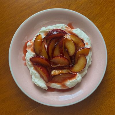Whipped cream topped with cooked plums on a pink plate.
