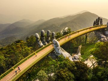 Golden Bridge held by giant stone hands in a lush mountainous landscape.