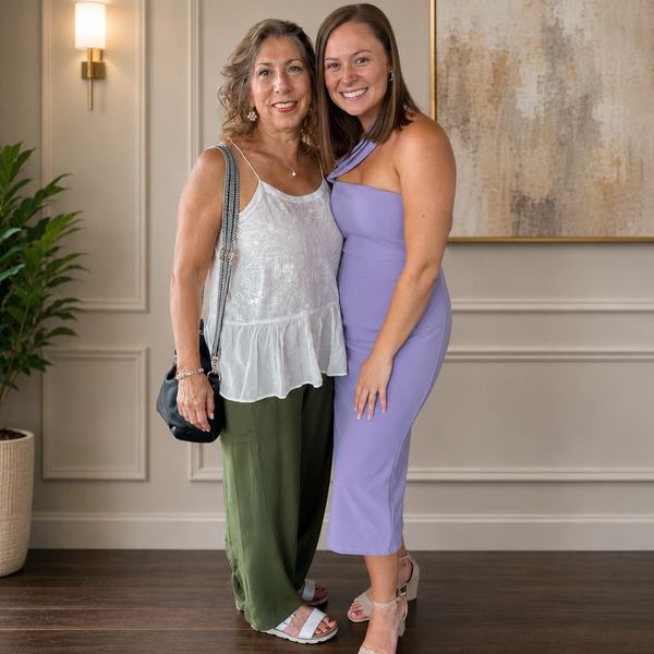 Two women smiling together in stylish outfits, posing indoors.