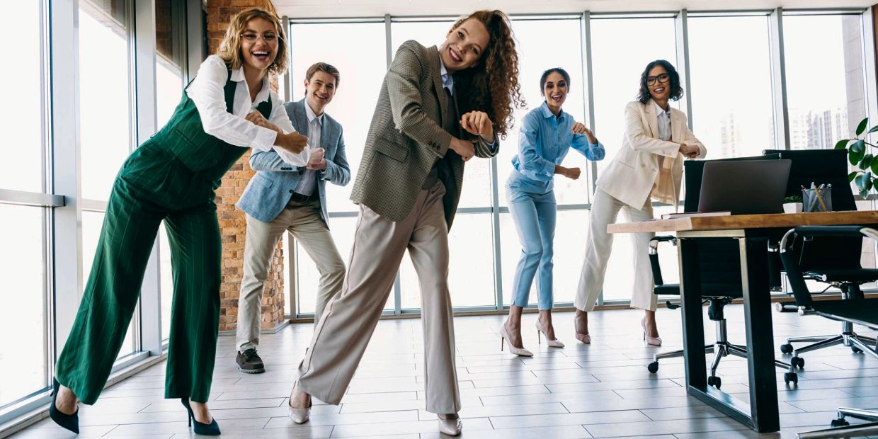 A group of five professionals dancing joyfully in a modern office space.