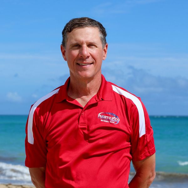 Man in red Puerto Rico National Team polo shirt standing by the sea.