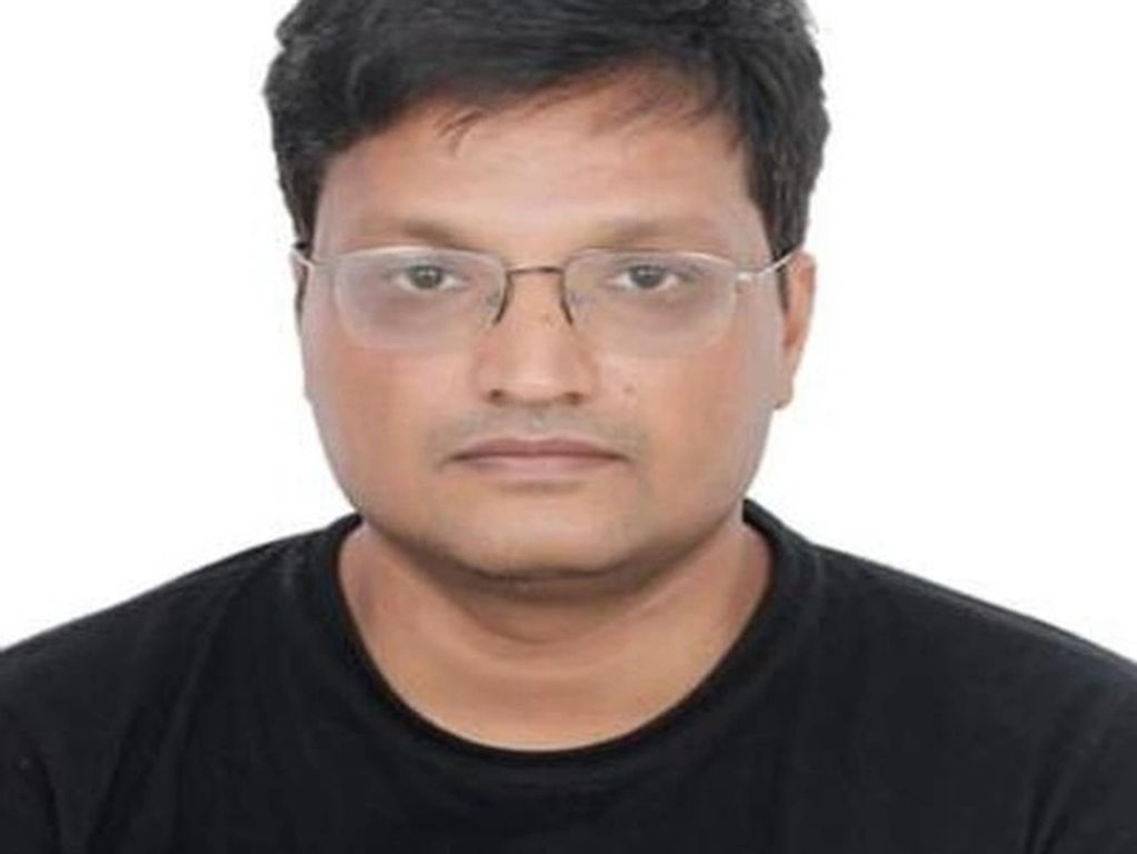 Portrait of a man wearing glasses and a black shirt against a white background.