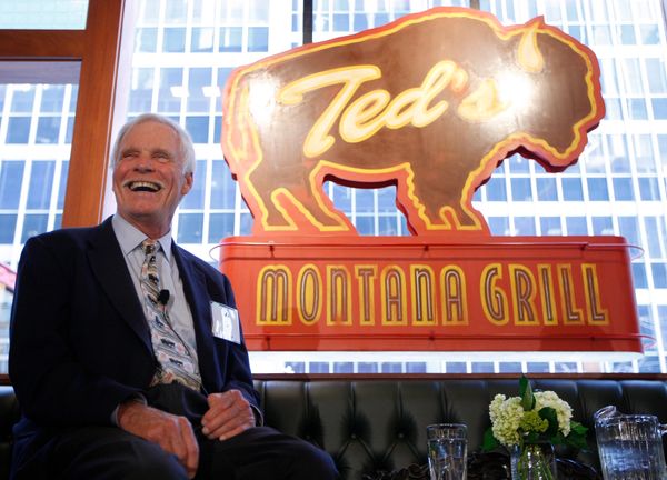 Smiling man in a suit at Ted's Montana Grill with a buffalo logo in the background.